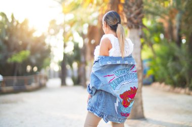 Kot ceket giyen genç ve güzel bir kadın kasabanın parkında ters duruyor.