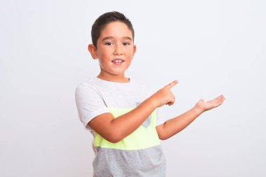 İzole edilmiş beyaz arka plan üzerinde duran sıradan tişört giyen güzel çocuk kameraya hayret ediyor ve gülümsüyor..