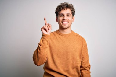 Sarışın, kıvırcık saçlı, beyaz arka planda sıradan süveter giyen, parlak fikirli genç bir adam. Heyecanlı ve mutlu. Bir numara..