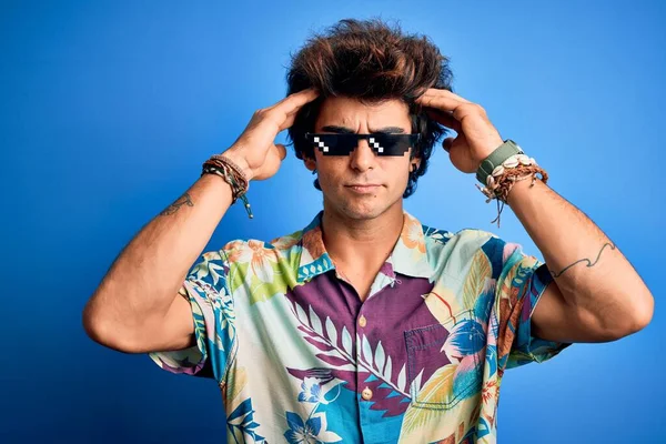 Young handsome man wearing thug life glasses standing over isolated blue background suffering from headache desperate and stressed because pain and migraine. Hands on head.