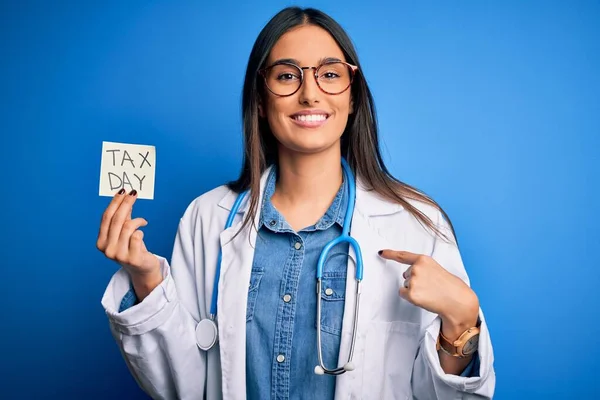 年轻的女医生戴着听诊器 手里拿着印有收税日信息的纸 满脸惊讶地指着自己 — 图库照片