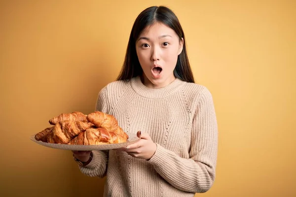 Młoda Azjatycka Kobieta Trzymając Francuskie Ciasto Croissant Żółtym Odizolowanym Tle — Zdjęcie stockowe