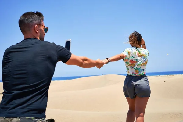 Young beautiful couple,  standing backwards making photo at the beach