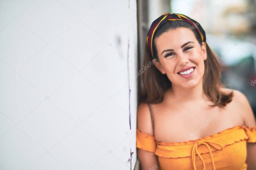 Young beautiful girl smiling happy and confident walking at the town street, standing with a smile on face leaning on the wall