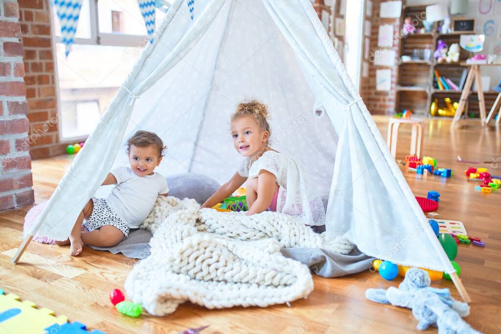 Beautiful toddlers playing inside tipi over blanket around lots of toys at kindergarten