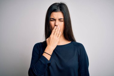 Young beautiful brunette woman wearing casual sweater standing over white background bored yawning tired covering mouth with hand. Restless and sleepiness.