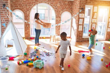 Anaokulunda bir sürü oyuncağın etrafında basketbol oynayan genç ve güzel öğretmenler ve yeni yürümeye başlayan çocuklar.