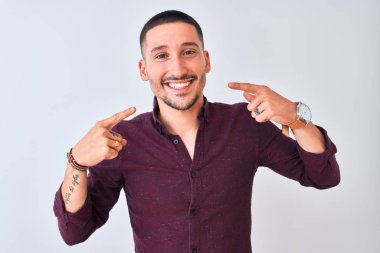 Genç yakışıklı iş adamı izole edilmiş arka planda durup neşeli bir şekilde gülümseyerek parmakları ve ağızlarıyla işaret ediyor. Diş sağlığı konsepti.