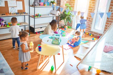 Güzel öğretmen ve bir grup çocuk anaokulunda bir sürü oyuncakla oynuyorlar.