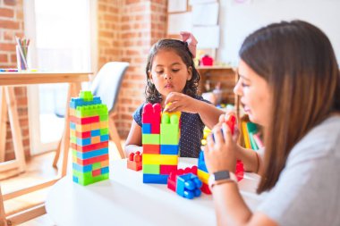 Güzel öğretmen ve küçük kız anaokulunda inşaat bloklarıyla oynuyorlar.