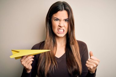 Güzel bir kız, elinde kağıt uçakla izole edilmiş beyaz arka planda dikiliyor. Öfkeyle bağırıyor, çıldırıyor ve öfkeyle bağırıyor.