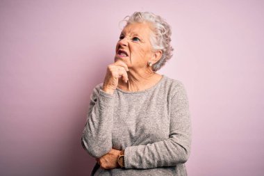Senior beautiful woman wearing casual t-shirt standing over isolated pink background Thinking worried about a question, concerned and nervous with hand on chin