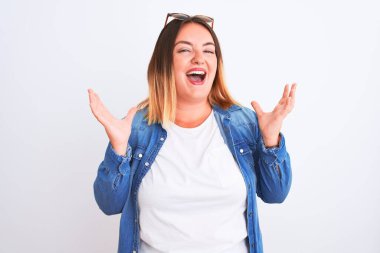 Beautiful woman wearing denim shirt standing over isolated white background celebrating crazy and amazed for success with arms raised and open eyes screaming excited. Winner concept
