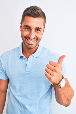 Young handsome elegant man wearing blue t-shirt over isolated background happy with big smile doing ok sign, thumb up with fingers, excellent sign