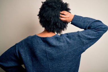 Young beautiful African American afro woman with curly hair wearing casual sweater Backwards thinking about doubt with hand on head