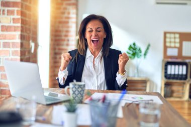 Middle age beautiful businesswoman working using laptop at the office celebrating surprised and amazed for success with arms raised and open eyes. Winner concept.