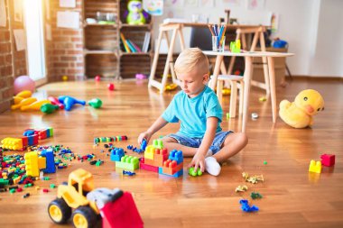 Anaokulunda oyuncak bloklarıyla oynayan beyaz bir çocuk. Anaokulu çocuğu oyun odasında kule inşa etmekten mutlu.