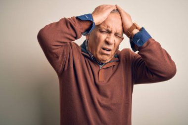 Üst düzey yakışıklı adam zarif bir süveter giyerek izole edilmiş beyaz arka planda dikiliyor. Baş ağrısı yüzünden çaresiz ve stresli. Çünkü acı ve migren. Ellerini başının üstüne koy..