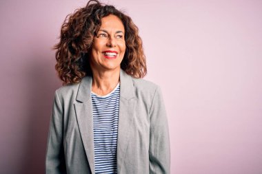 Middle age beautiful businesswoman wearing elegant jacket over isolated pink background looking away to side with smile on face, natural expression. Laughing confident.