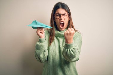 Gri arka plan üzerinde duran kağıttan bir uçak tutan genç bir kadın öfkeyle bağırıyor, deliriyor ve öfkeyle bağırıyor.