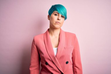 Young beautiful businesswoman with blue fashion hair wearing jacket over pink background Relaxed with serious expression on face. Simple and natural looking at the camera.