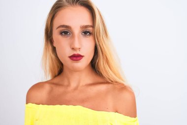 Sarı tişört giyen genç güzel bir kadın izole edilmiş beyaz arka planda duruyor. Akıllı bir yüz ifadesiyle ciddi ciddi düşünüyor.