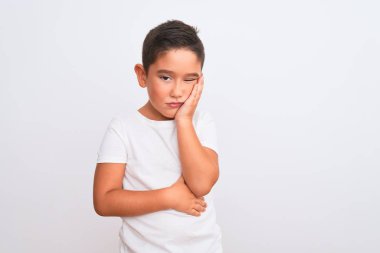 Güzel çocuk, izole edilmiş beyaz arka plan üzerinde duran sıradan bir tişört giyip kollarını kavuşturarak depresyondan sıkılmış ve yorgun görünüyor..
