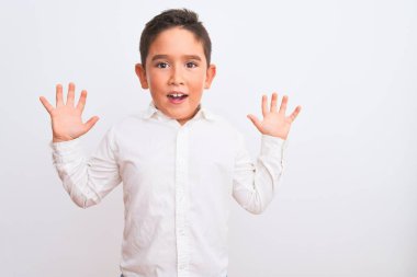 Beautiful kid boy wearing elegant shirt standing over isolated white background celebrating crazy and amazed for success with arms raised and open eyes screaming excited. Winner concept