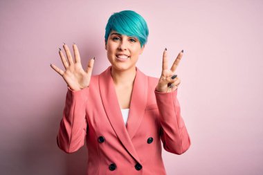 Young beautiful businesswoman with blue fashion hair wearing jacket over pink background showing and pointing up with fingers number seven while smiling confident and happy.