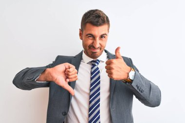 Young handsome business man wearing suit and tie over isolated background Doing thumbs up and down, disagreement and agreement expression. Crazy conflict