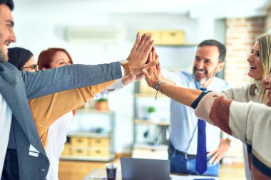 Bir grup işçi el ele tutuşup ofiste beşlik çakıyor.