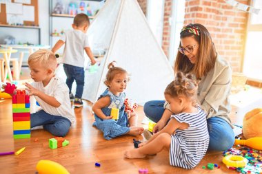 Güzel öğretmen ve bir grup çocuk anaokulunda bir sürü oyuncakla oynuyorlar.