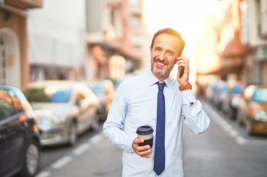 Orta yaşlı yakışıklı işadamı akıllı telefondan konuşuyor. İçiyor, kahveyi götürüyor, gülümsüyor.