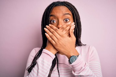 Close up of young african american woman wearing pink sweater over isolated background shocked covering mouth with hands for mistake. Secret concept.