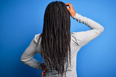 Young african american woman standing wearing casual turtleneck over blue isolated background Backwards thinking about doubt with hand on head