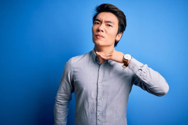 Genç yakışıklı Çinli bir adam, günlük gömleğini giymiş, mavi arka planda dikiliyor, boğazını bıçak gibi kesiyor, saldırganlığı şiddetli bir şiddetle tehdit ediyor.