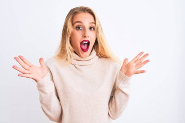 Balıkçı yaka kazak giyen genç ve güzel bir kadın izole edilmiş beyaz arka planda durmuş çılgın ve başarıyı kutlarken kolları havada ve gözleri açık heyecanlı bir şekilde haykırıyorlardı. Kazanan konsept