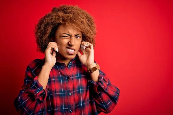 若い美しいアフリカ系アメリカ人のアフロ女性は 大きな音楽のノイズのためにいらいらした表情で指で耳を覆うカジュアルなシャツを着ています ろう者の概念 — ストック写真