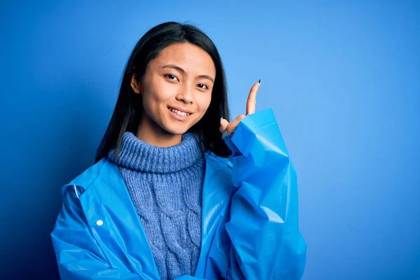 Young Beautiful Chinese Woman Wearing Rain Coat Standing Isolated Blue — 스톡 사진