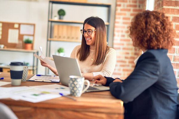 Two beautiful businesswomen smiling happy and confident. Sitting with smile on face working together using laptop at the office