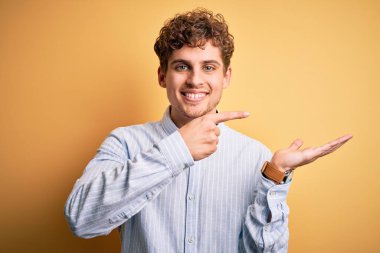 Sarışın, kıvırcık saçlı, sarı arka planda çizgili tişört giyen genç, yakışıklı bir adam kameraya hayret ediyor ve gülümsüyor..