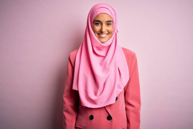 Pembe Müslüman başörtüsü ve mutlu ve havalı bir gülümsemesi olan iş ceketi giyen genç, güzel esmer iş kadını. Şanslı kişi..