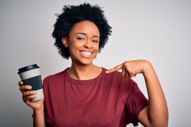 Young African American afro woman with curly hair drinking cup of coffee with surprise face pointing finger to himself