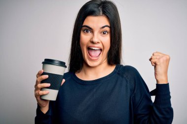 Genç, güzel esmer kadın izole edilmiş beyaz arka planda bir fincan kahve içiyor. Gururla bağırıyor, zaferi kutluyor ve başarıyı kutluyor. Çok heyecanlı, coşkulu bir duygu.