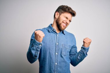 Sakallı, mavi gözlü, çok mutlu ve heyecanlı genç sarışın adam kolları havada, gülümseyen ve başarı için bağıran kazanan jestler yapıyor. Kutlama konsepti.