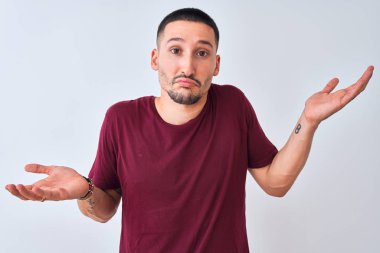 Soyutlanmış arka planda duran genç yakışıklı adam elleri ve kolları havada, kafası karışmış bir ifade takınıyor. Şüphe kavramı.