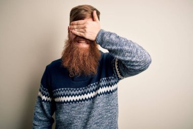 Sakallı, kışın süveter giyen yakışıklı kızıl saçlı, soyutlanmış arka planda gülümseyen ve yüzünde şaşkınlıkla gülümseyen yakışıklı bir adam. Kör kavram.