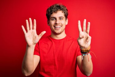 Sarışın, kıvırcık saçlı, kırmızı arka planda sıradan tişörtler giyen ve 8 numarayı işaret eden, kendinden emin ve mutlu gülümseyen genç bir adam..