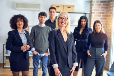 Bir grup iş adamı mutlu ve kendinden emin gülümsüyor. Birlikte poz verip kameraya bakıyoruz. Orta yaşlı, güzel bir kadın. Ofiste gülümsüyor.