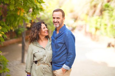 Şehir parkında mutlu ve kendinden emin gülümseyen orta yaşlı güzel bir çift. Yüzünde gülümsemeyle ayakta durup sarılarak